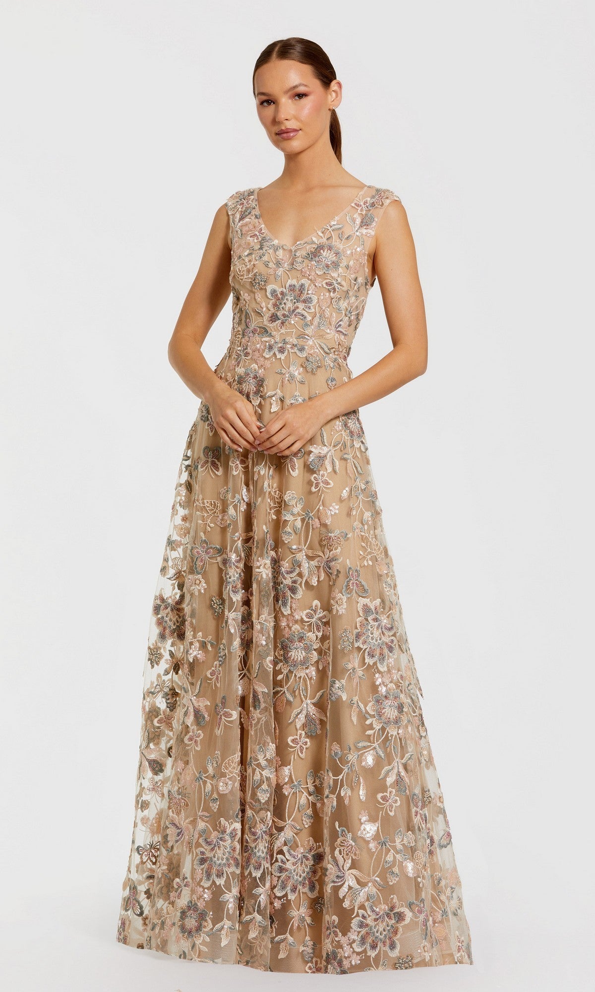 A woman stands against a plain white background wearing the Mac Duggal 68907 long formal dress in taupe, featuring a sleeveless, floor-length design with intricate floral lace embroidery.